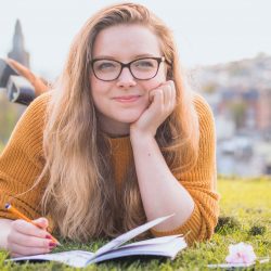 woman-lying-on-green-grass-while-holding-pencil-1458318
